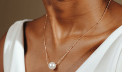 Person wearing a delicate gold chain necklace with a large white pearl pendant.