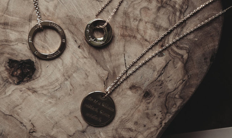 Three gold-colored pendant necklaces with engravings on a textured wooden surface.