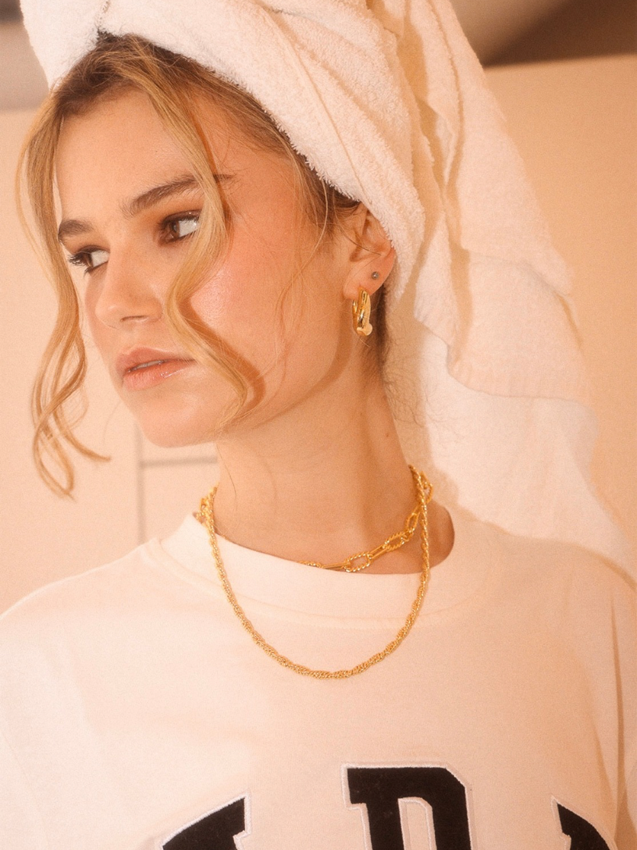 A woman with a towel on her head wears gold jewelry, including a Crossing Twisted Chain.