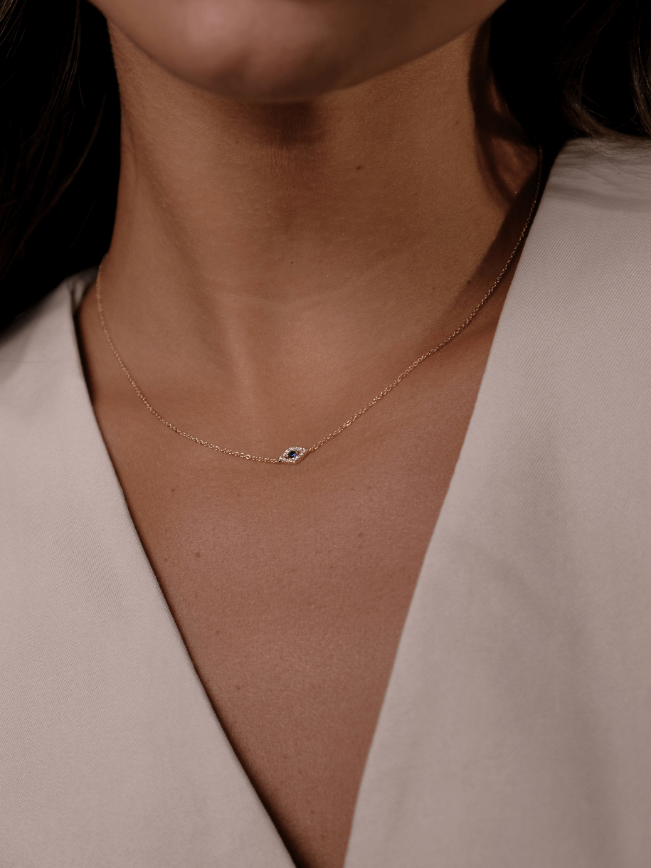Close-up of a woman's neck wearing The Petite Evil Eye gold chain necklace with an eye-shaped pendant.